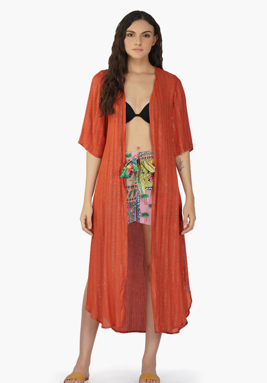 Woman wearing a long rust-colored kimono-style garment over a colorful swimsuit on a white background