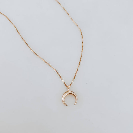 Gold necklace with a crescent moon pendant on a light gray background