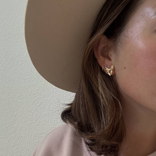 Close-up of a person wearing a gold earring with a neutral background