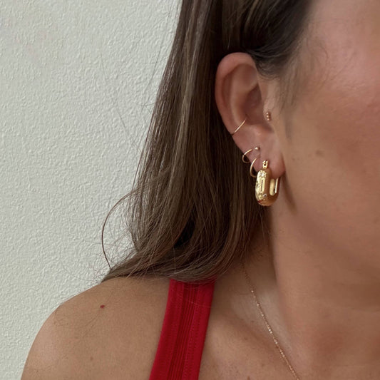 Close-up of a person wearing gold hoop earrings with a plain background