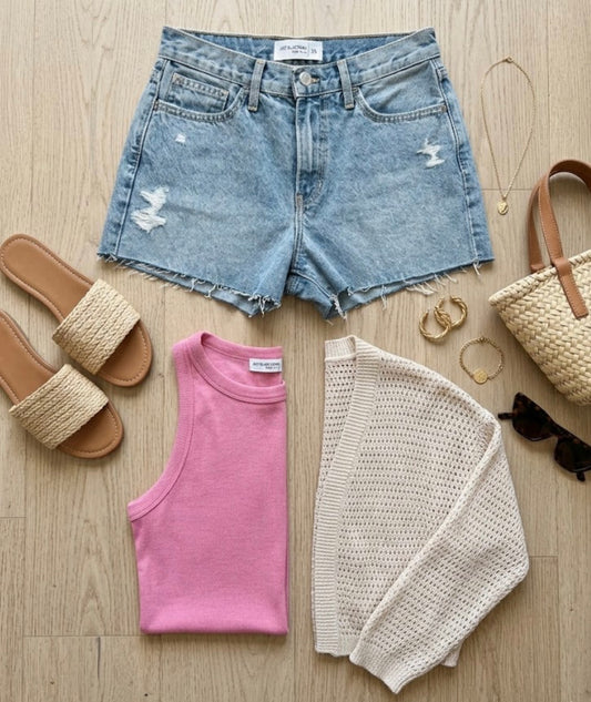 Denim shorts, pink tank top, beige cardigan, sandals, handbag, and jewelry on a wooden surface