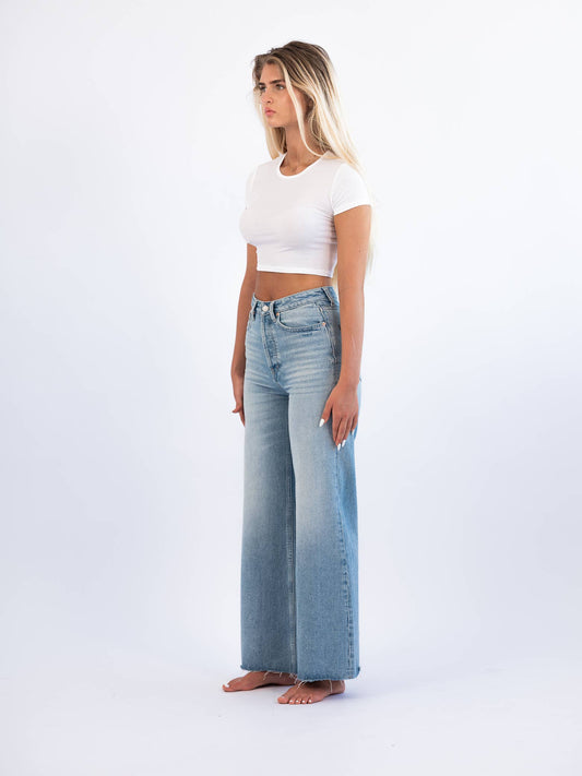 A female model wearing a white crop top and high-rise wide leg non-stretch denim jeans with a vintage inspired light wash and scissor cut hem.