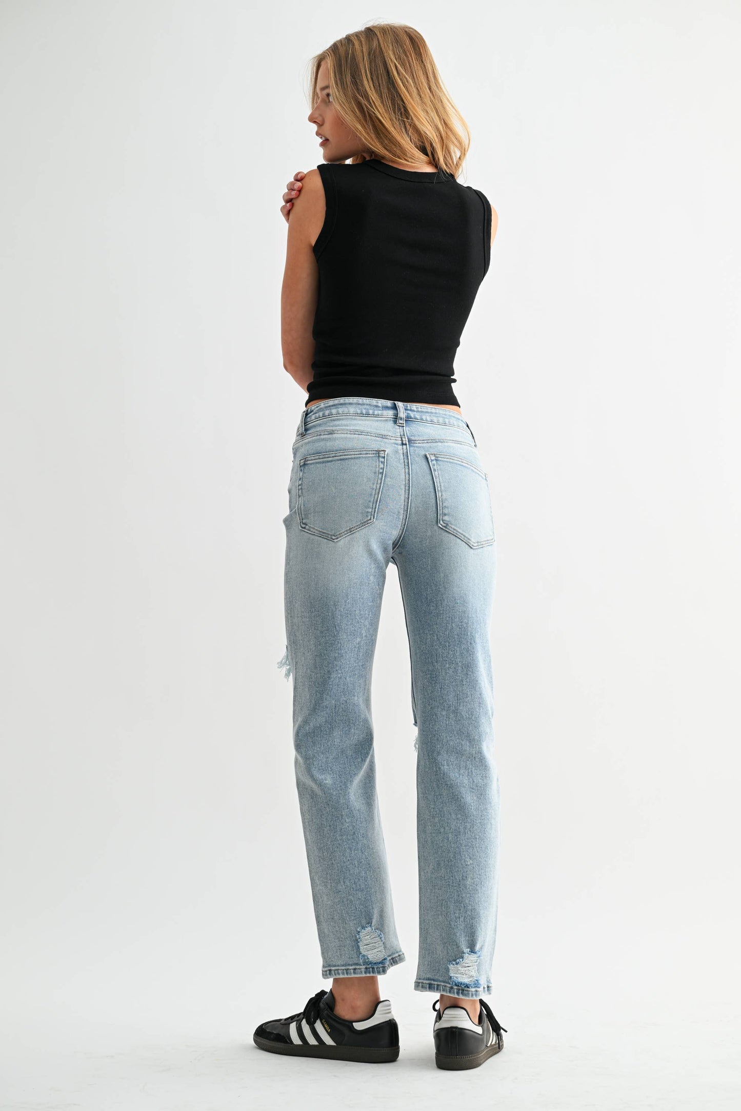 Woman wearing light blue jeans and a black top on a white background
