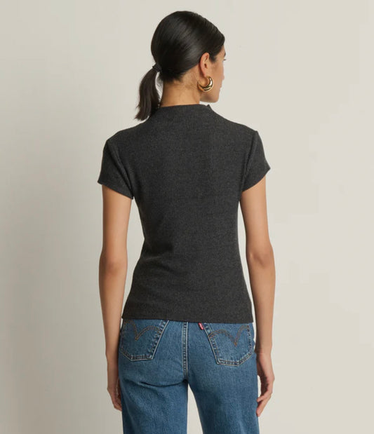 Woman wearing a dark gray t-shirt and blue jeans on a plain background