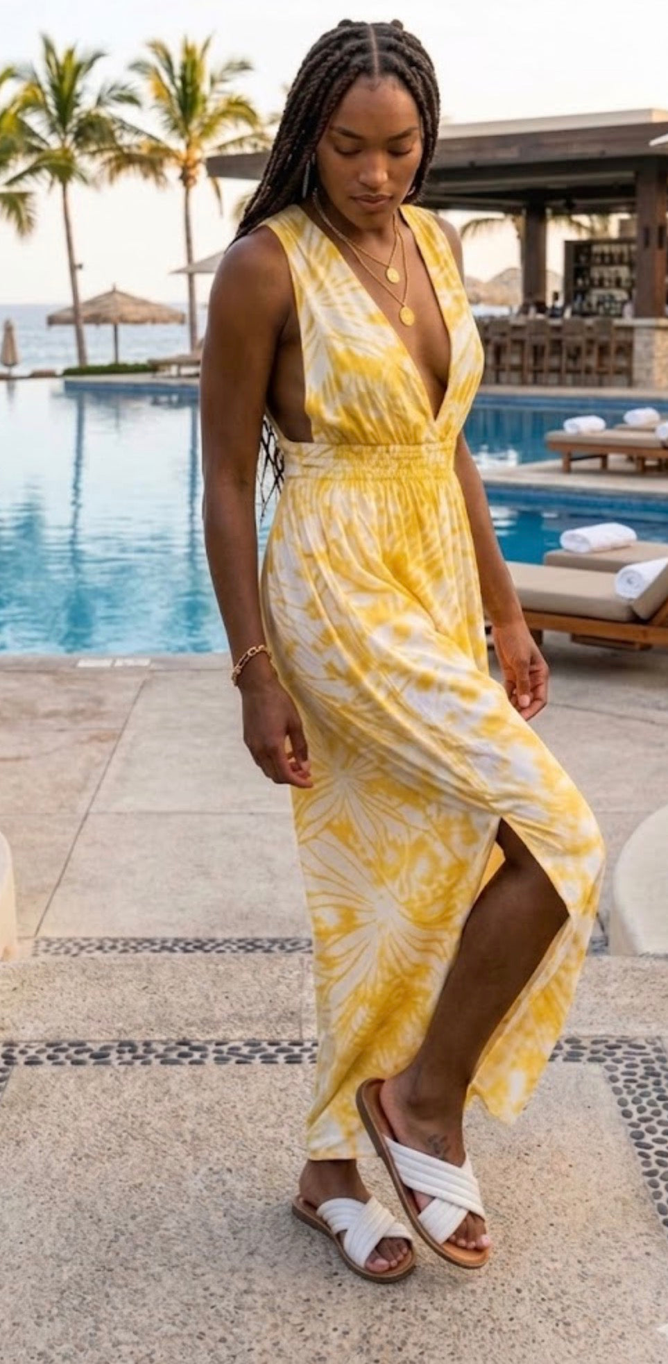Woman in a yellow dress standing by a poolside with palm trees in the background