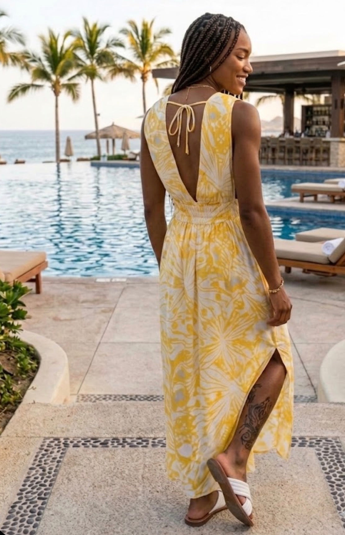 Woman in a yellow floral dress standing by a poolside with palm trees in the background