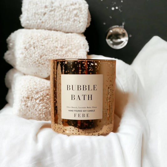 Candle labeled 'Bubble Bath' by FEBE with stacked white towels in the background