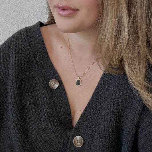Woman wearing a dark gray cardigan with buttons and a gold necklace.