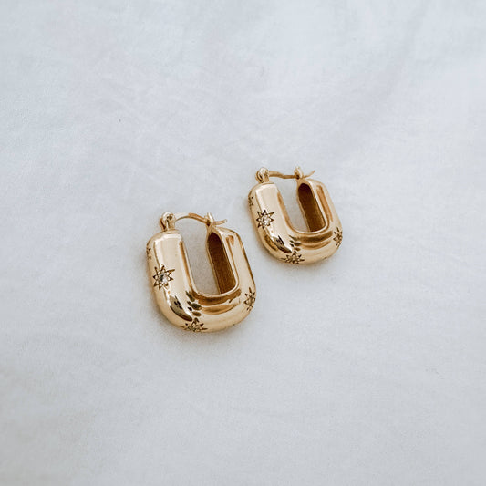 Gold hoop earrings with etched stars and tiny diamonds on a light gray background