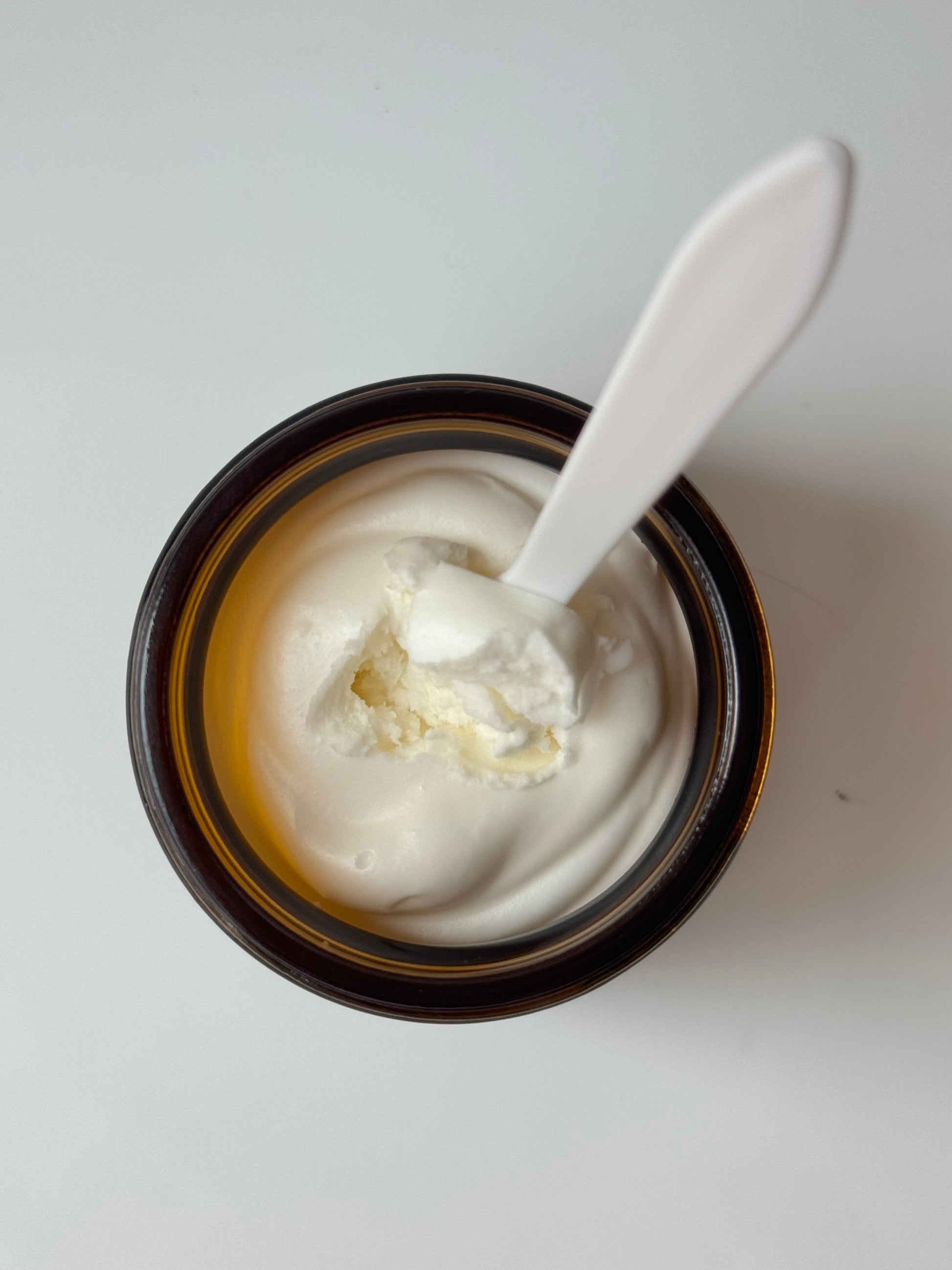 Jar of face cream with a spoon inside on a white background