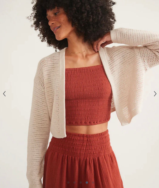 Woman wearing a beige cardigan over a rust-colored top and skirt on a white background