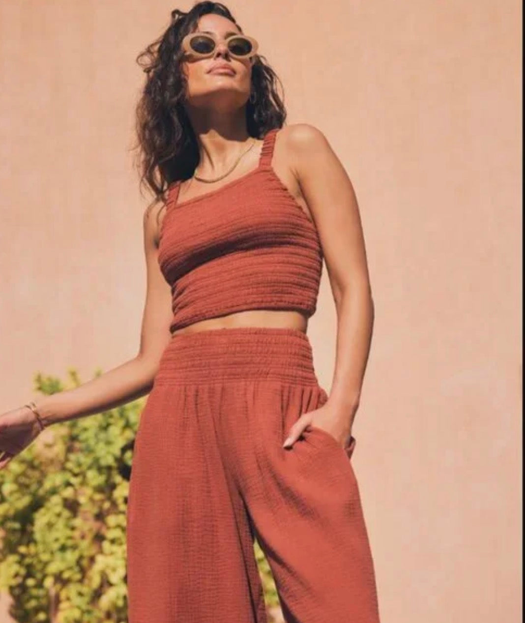 Woman wearing a rust-colored outfit with sunglasses against a beige wall.