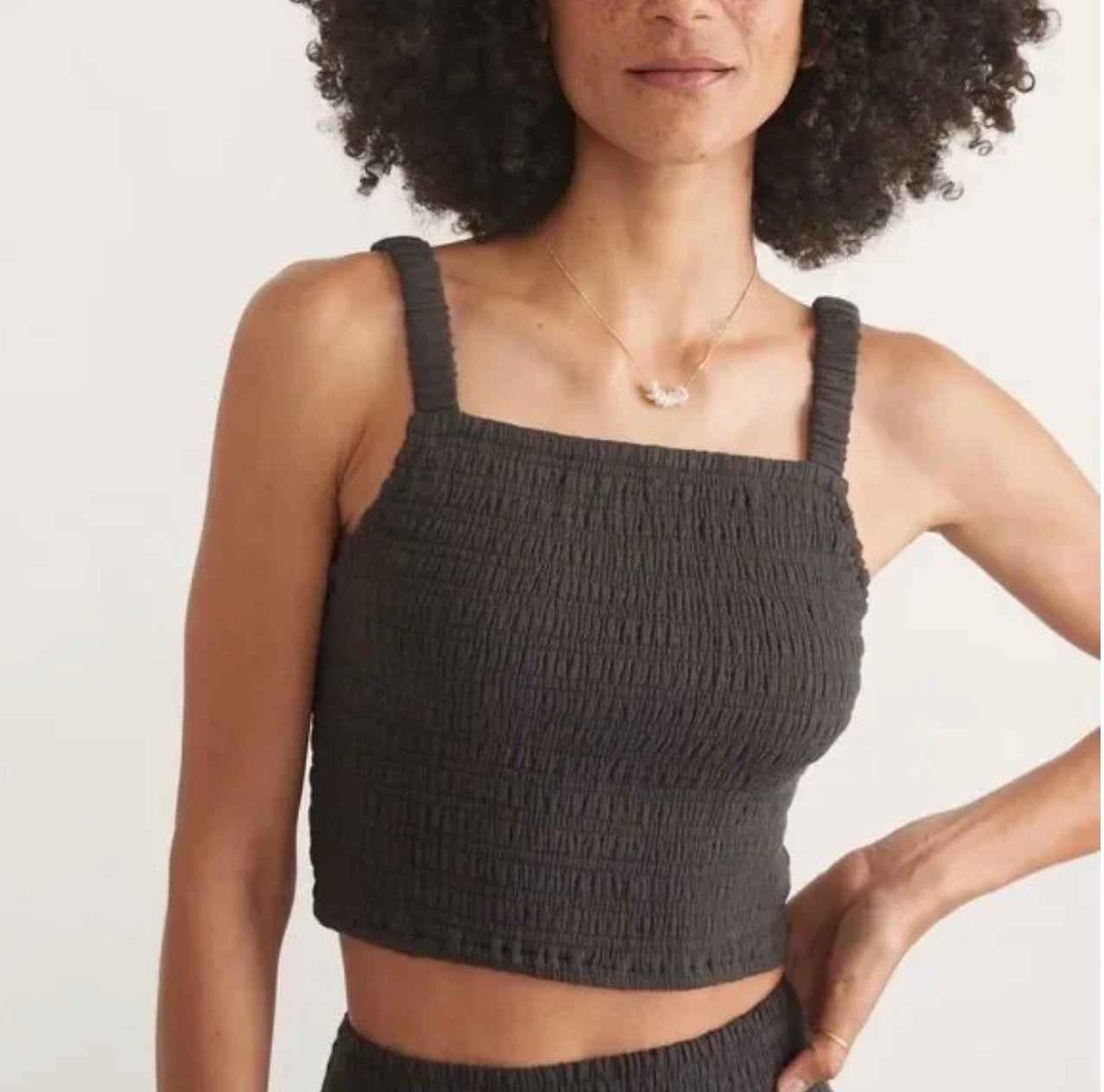 Woman wearing a dark gray ruched tank top against a plain background