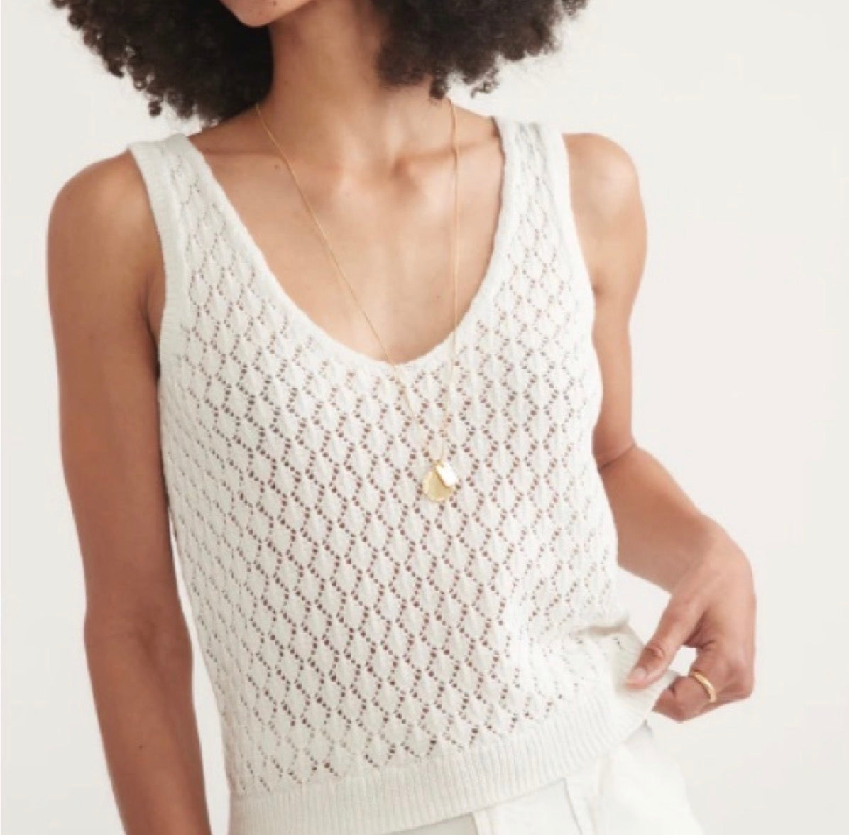 Woman wearing a white crochet tank top on a plain background