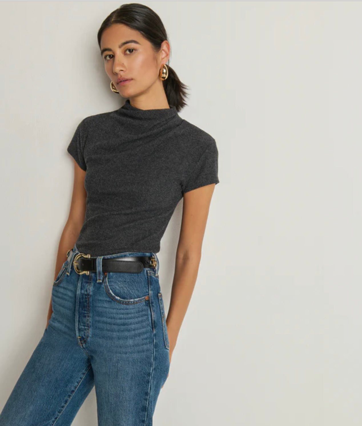 Woman wearing a dark gray t-shirt and blue jeans against a plain background