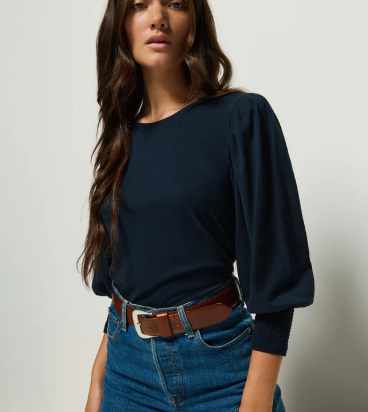 Woman wearing a navy blue Nation top and blue jeans with a brown belt 
