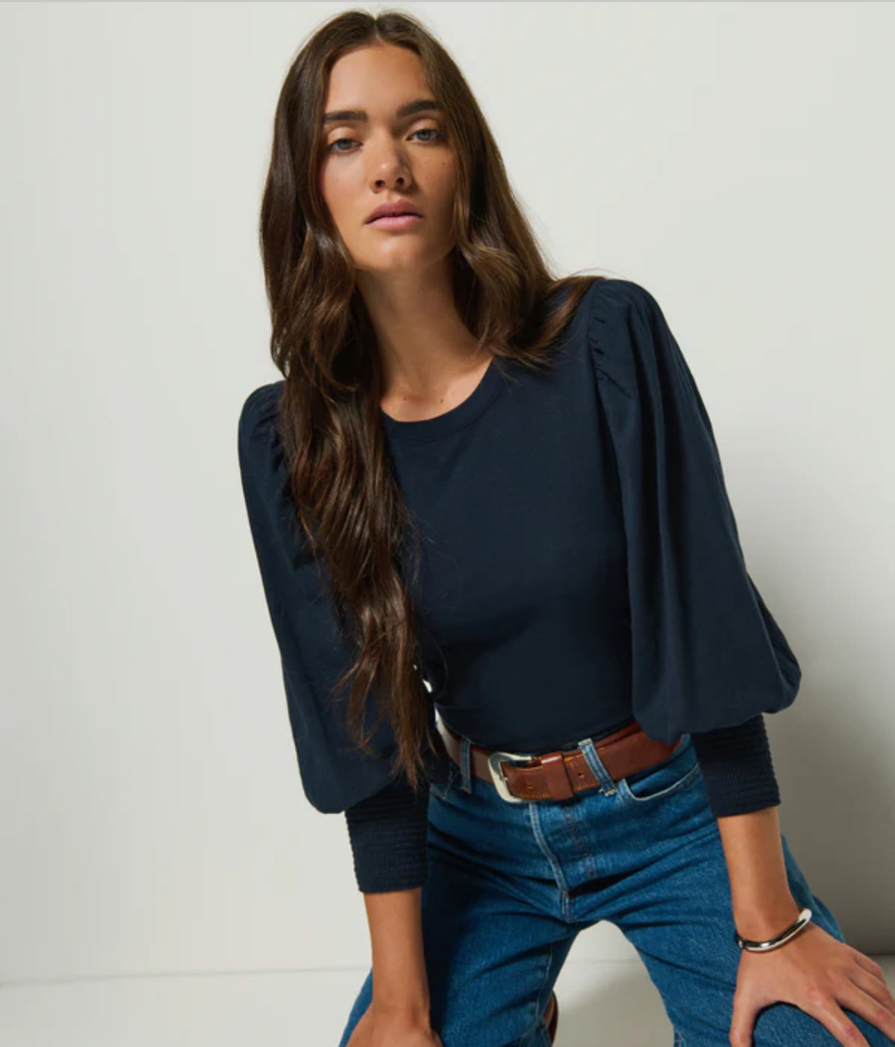 Woman wearing a navy blue top and blue jeans against a plain background