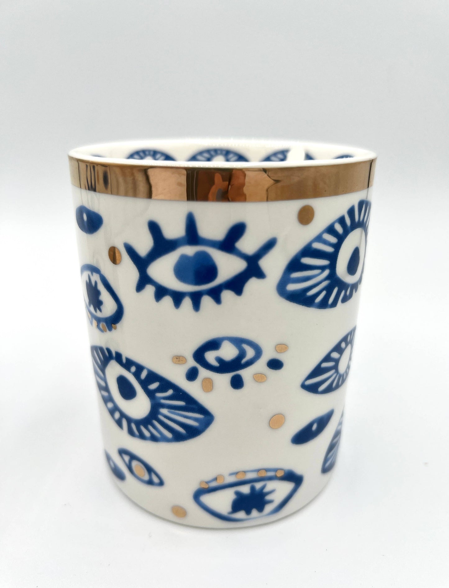 Ceramic mug with blue eye patterns and gold accents on a white background