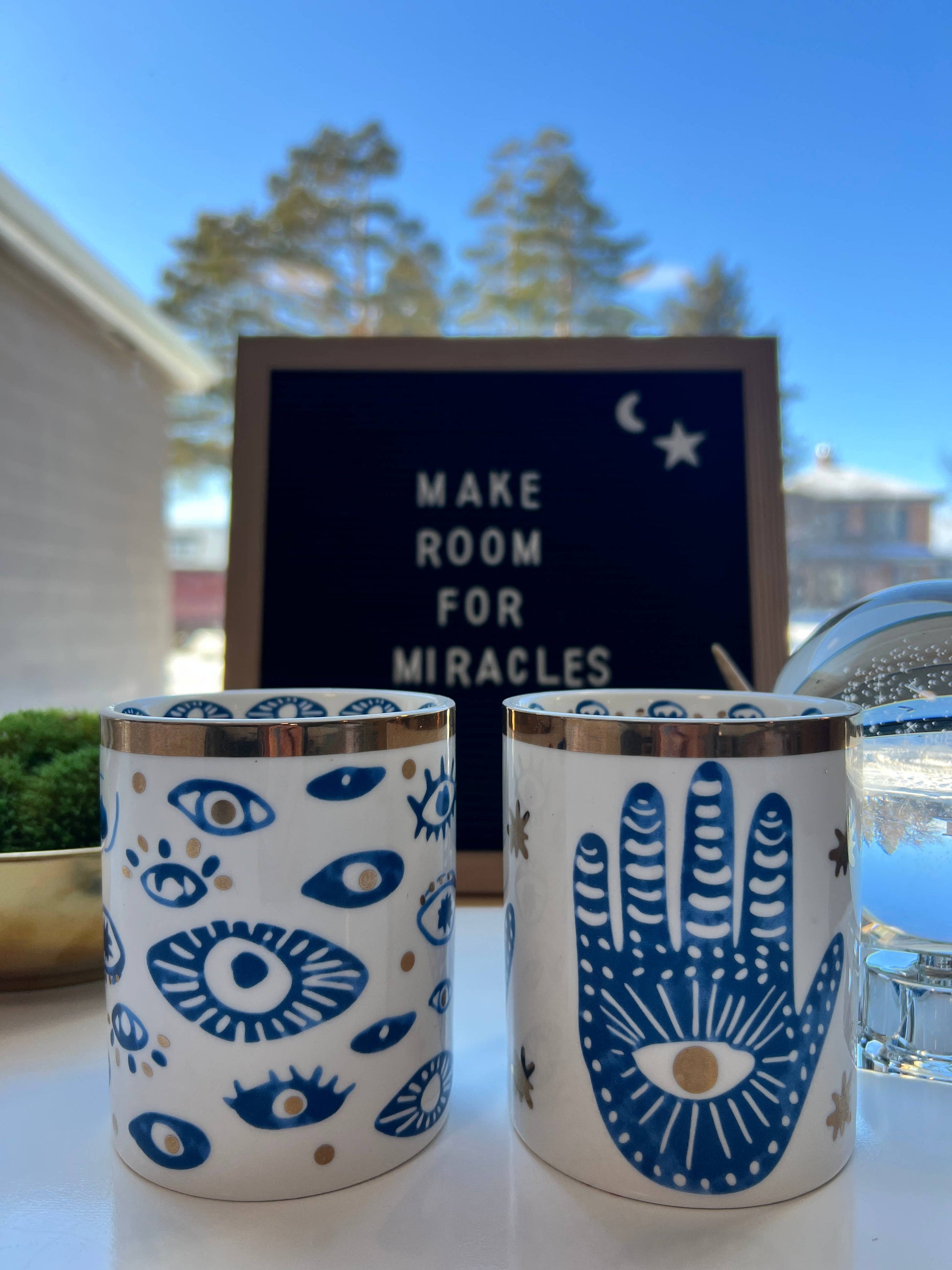 Two ceramic cups with blue designs on a surface with a sign in the background.