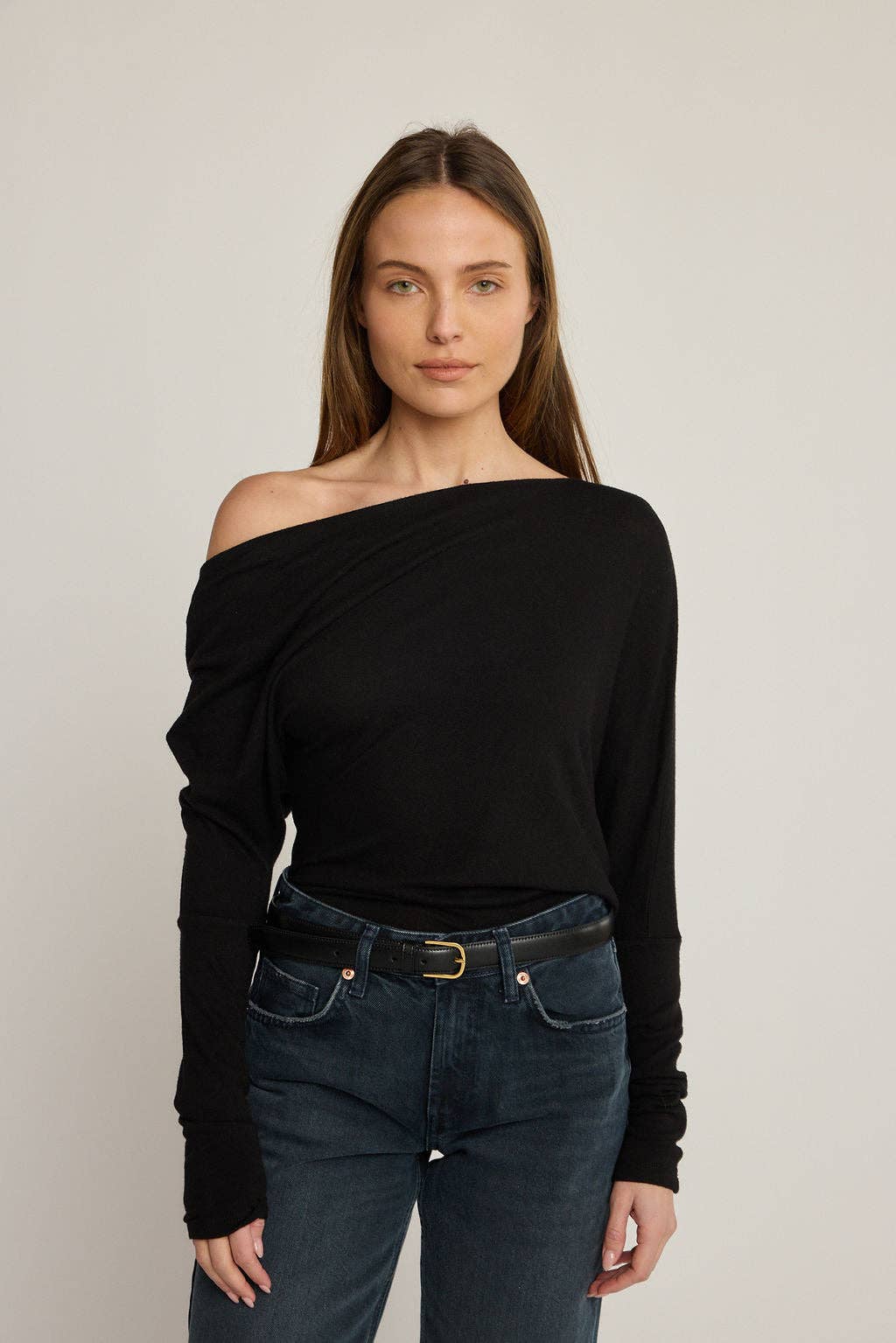 Woman wearing a black off-shoulder top and blue jeans against a plain background