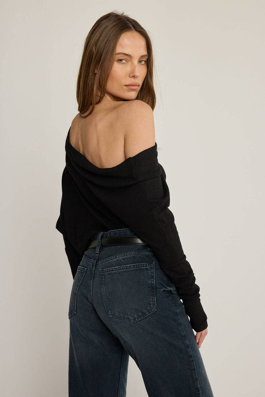 Woman wearing a black off-shoulder top and blue jeans against a plain background