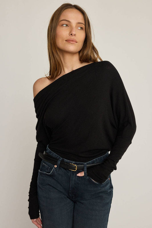 Woman wearing a black off-shoulder top and dark jeans against a plain background