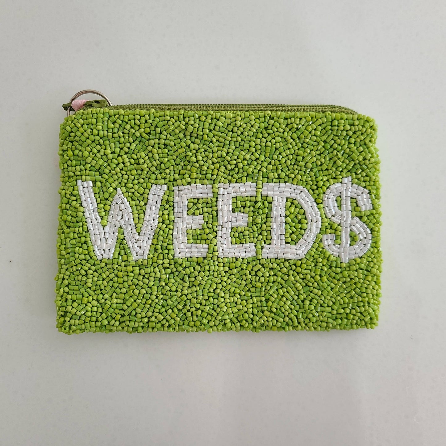 Green textured pouch with 'WEED$' text on a light gray background